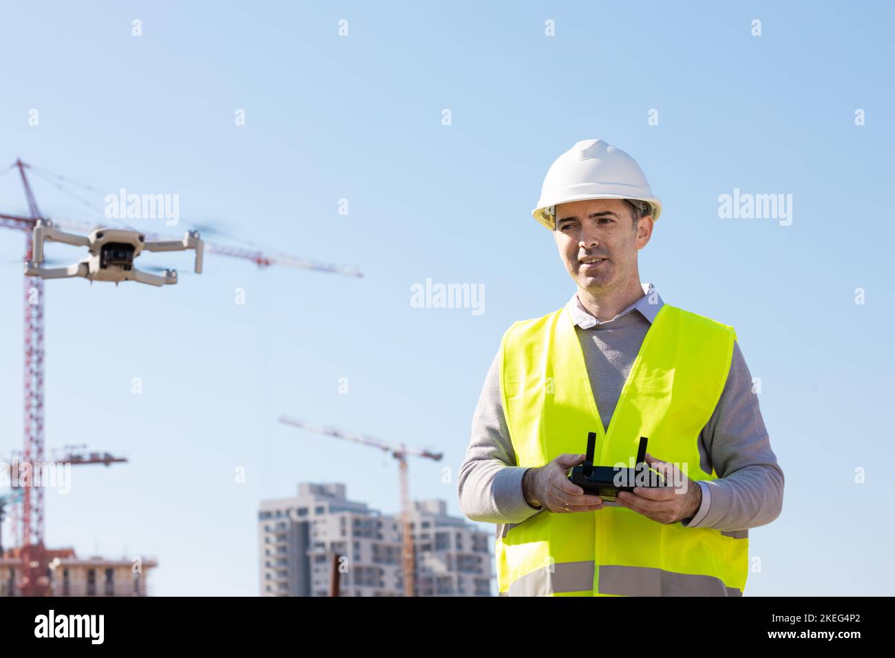 Man launches a quadcopter. An engineer flies a drone next to a construction site. Concept - construction observation with a drone.  Construction crane Stock Photo