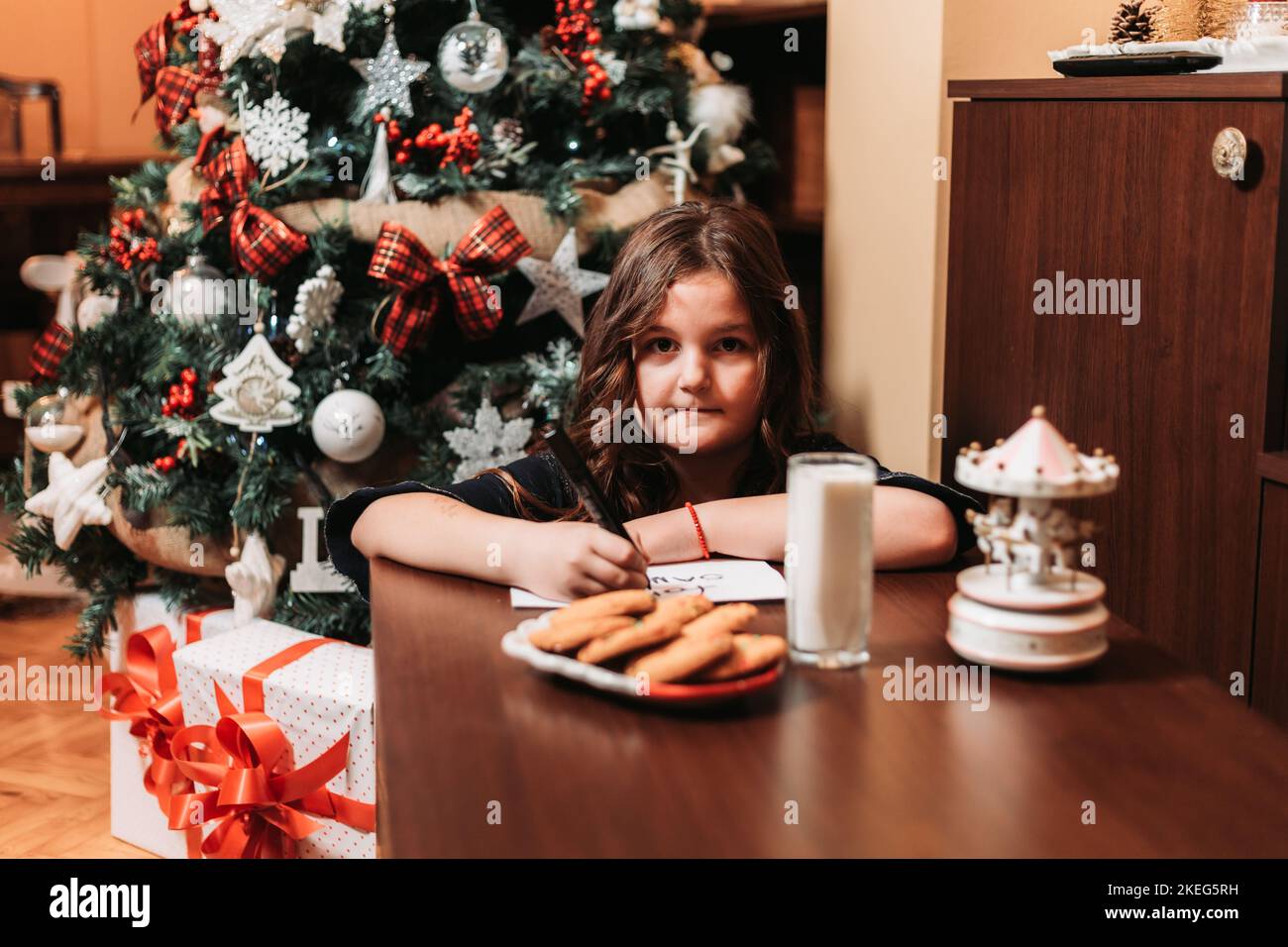 Little girl leaving cookies and glass of milk for Santa, writing him a