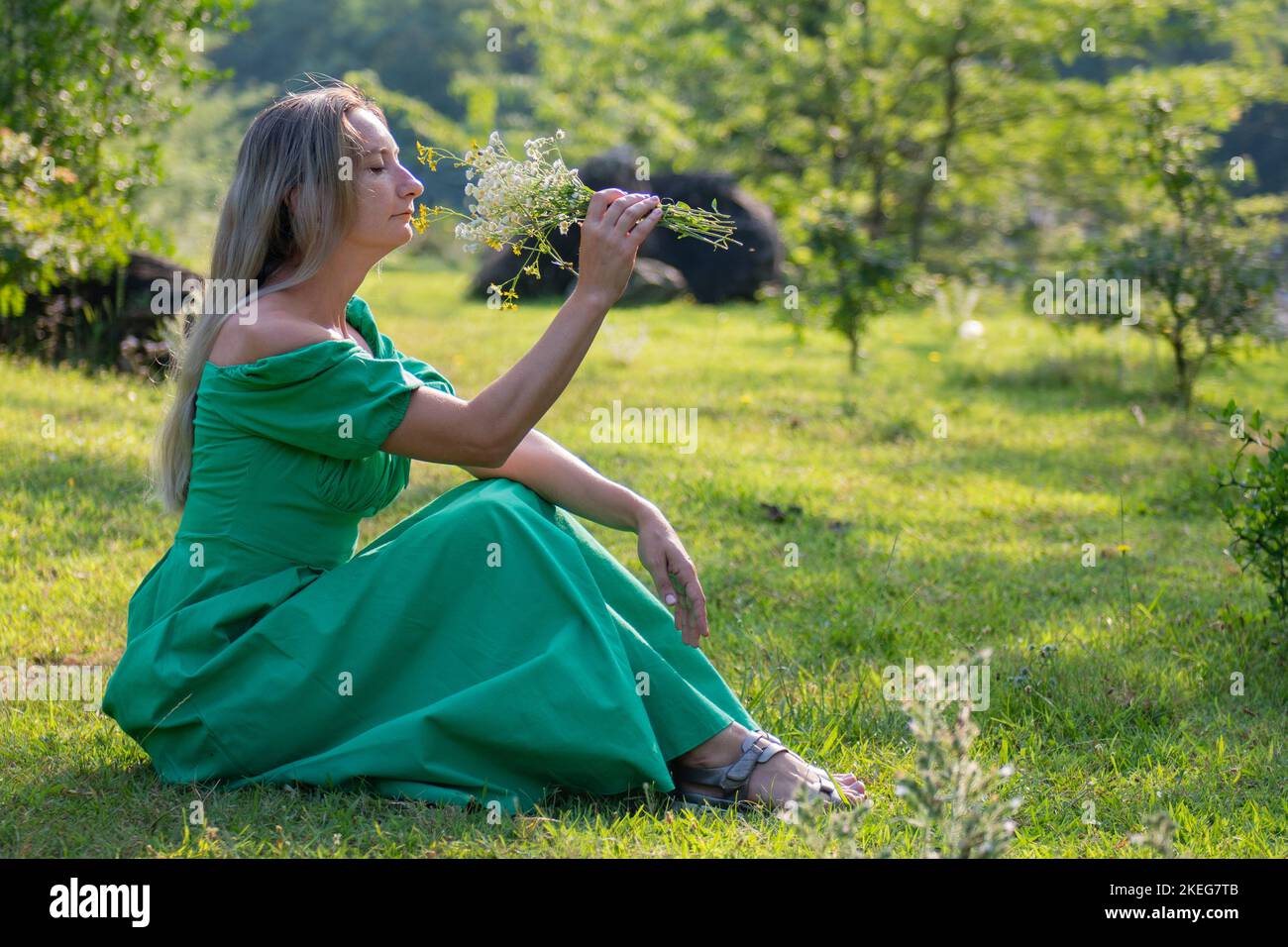 one woman is sitting on the grass with flowers in a green dress Stock ...