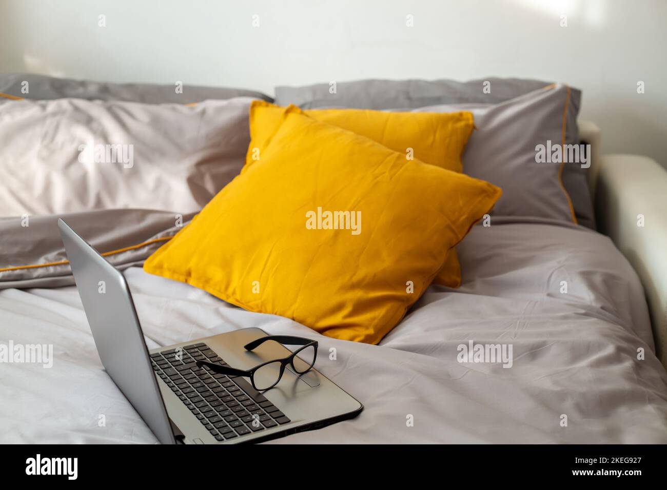 Workplace in bed. Laptop with glasses on the bed on gray bedding and