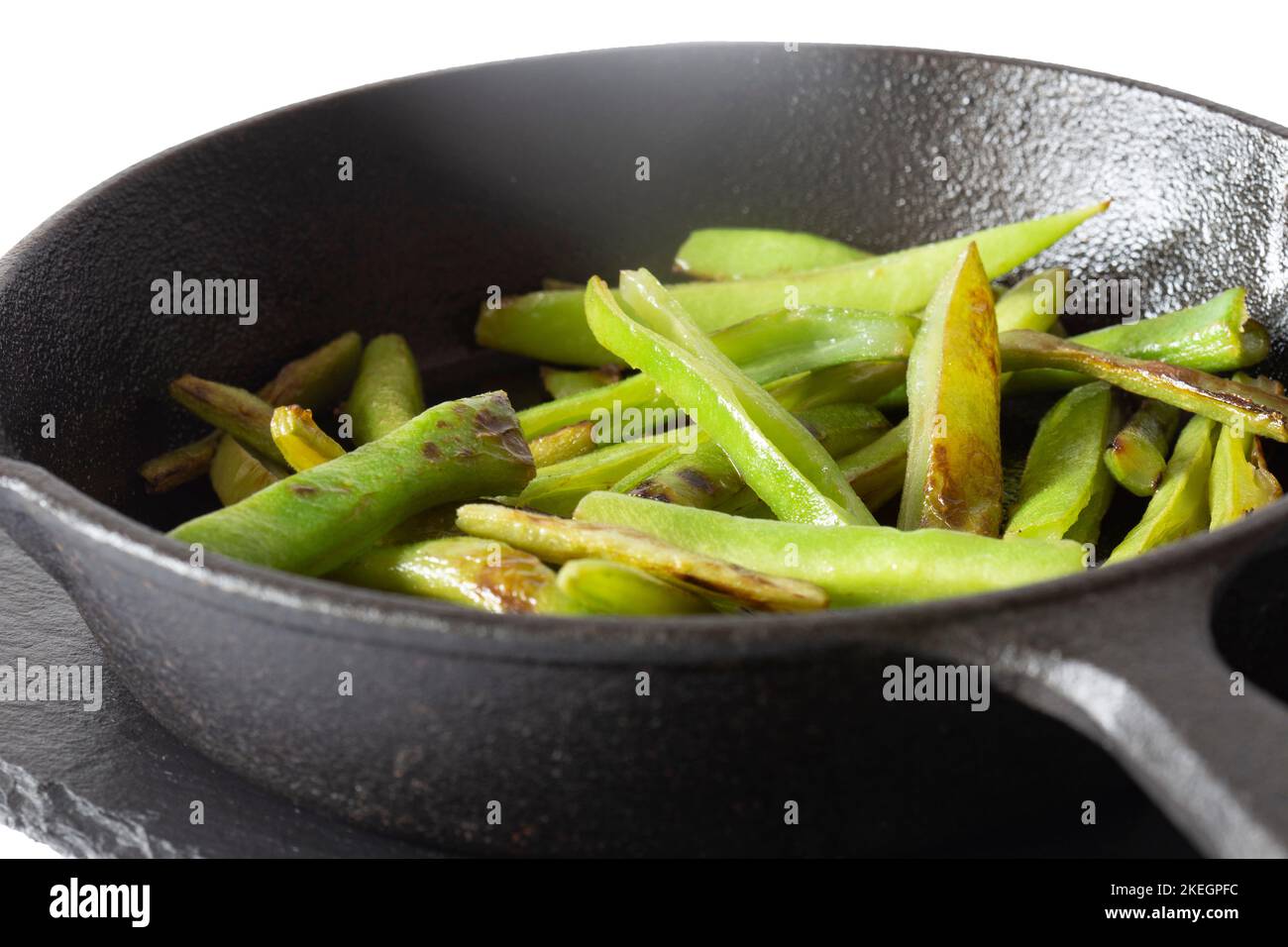 Green beans fried, in a cast iron frying pan wiyth olive oil, on a slate board. Isolated on a white background Stock Photo