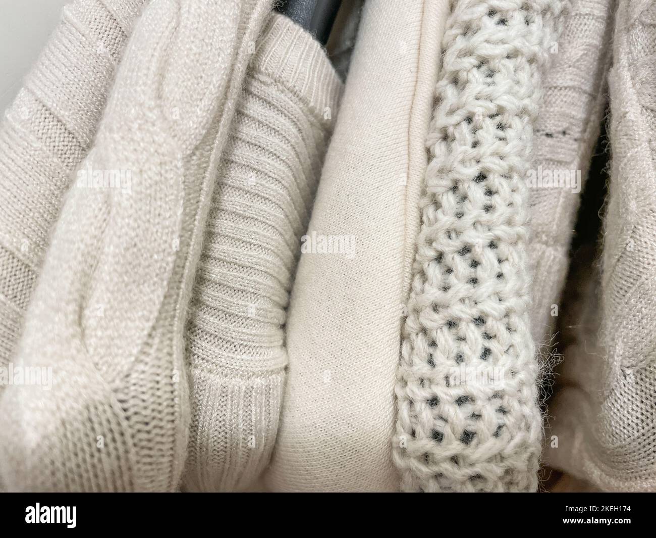 Knitted sweaters and jumpers of light beige cream color on hangers in stack photo from above. Fall Winter warm clothes store collection. Beige fashion Stock Photo
