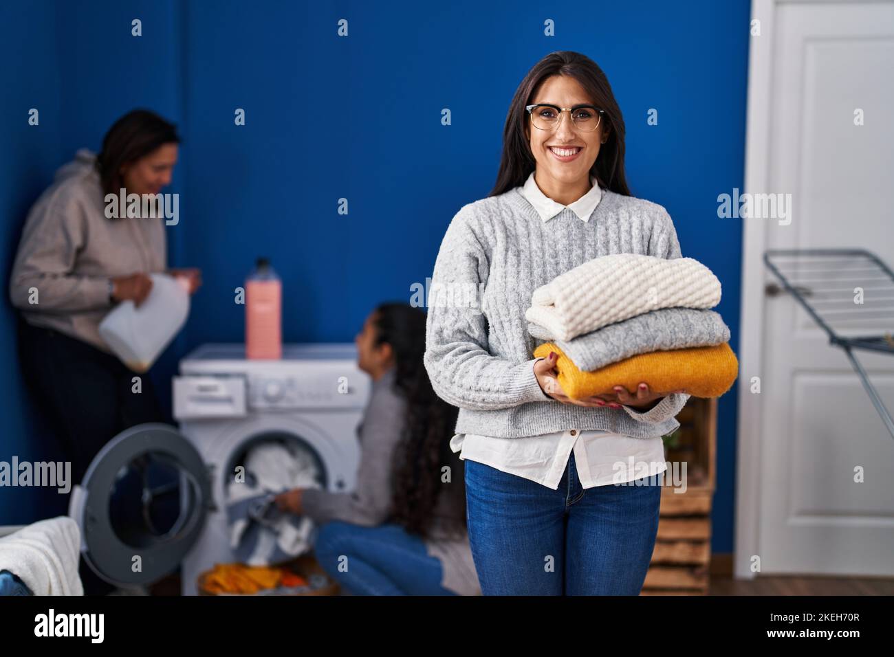 Three women doing laundry at home smiling with a happy and cool smile on face. showing teeth. Stock Photo