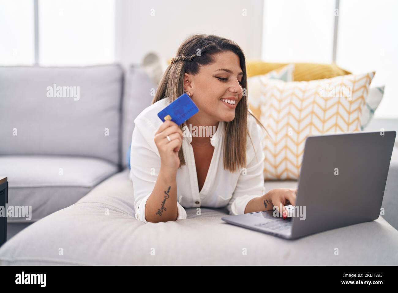 Young hispanic woman using laptop and credit card lying on sofa at home ...