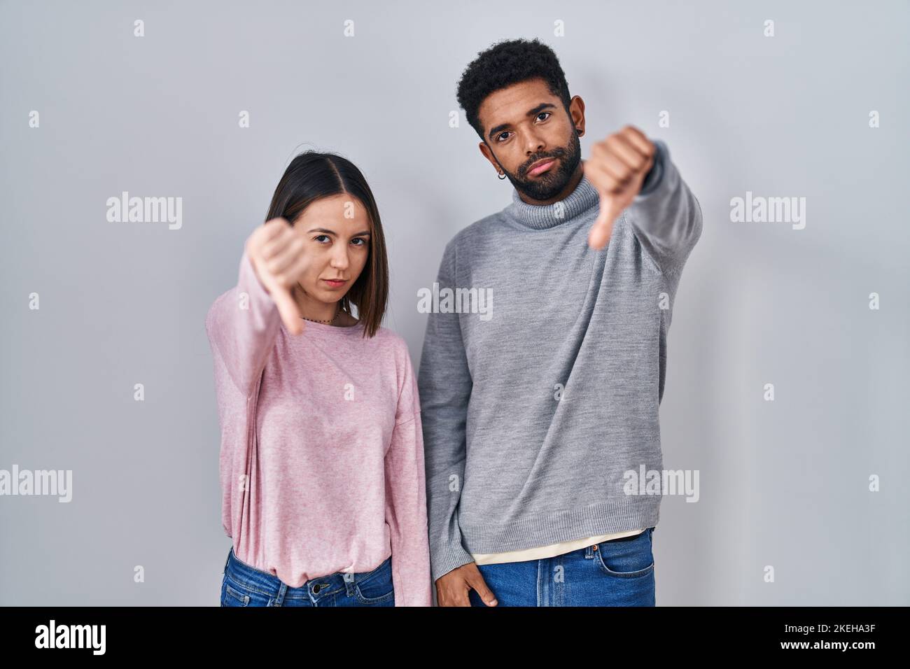 Young hispanic couple standing together looking unhappy and angry ...