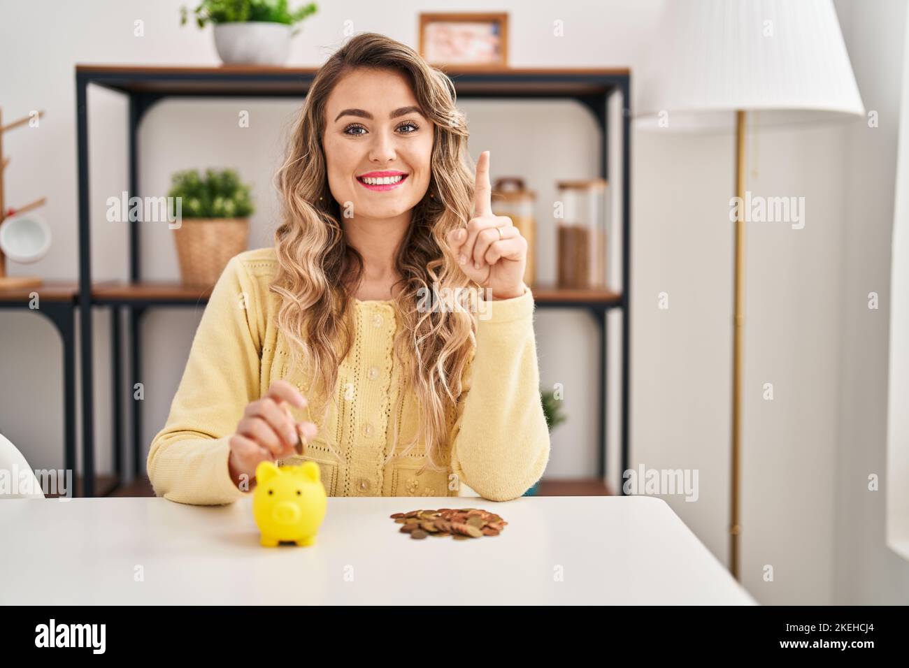 Young caucasian woman sitting on the table with piggy bank and coins ...