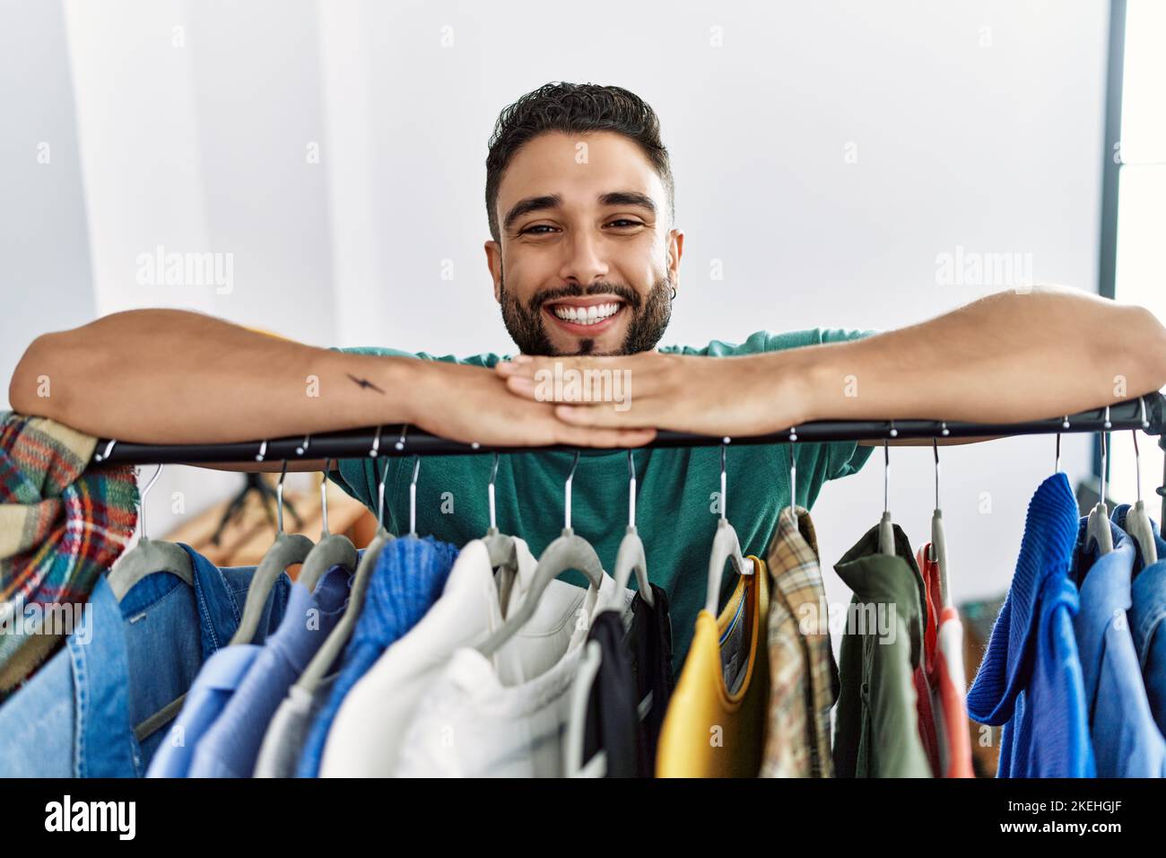 Young arab man customer smiling confident leaning on rack at clothing ...