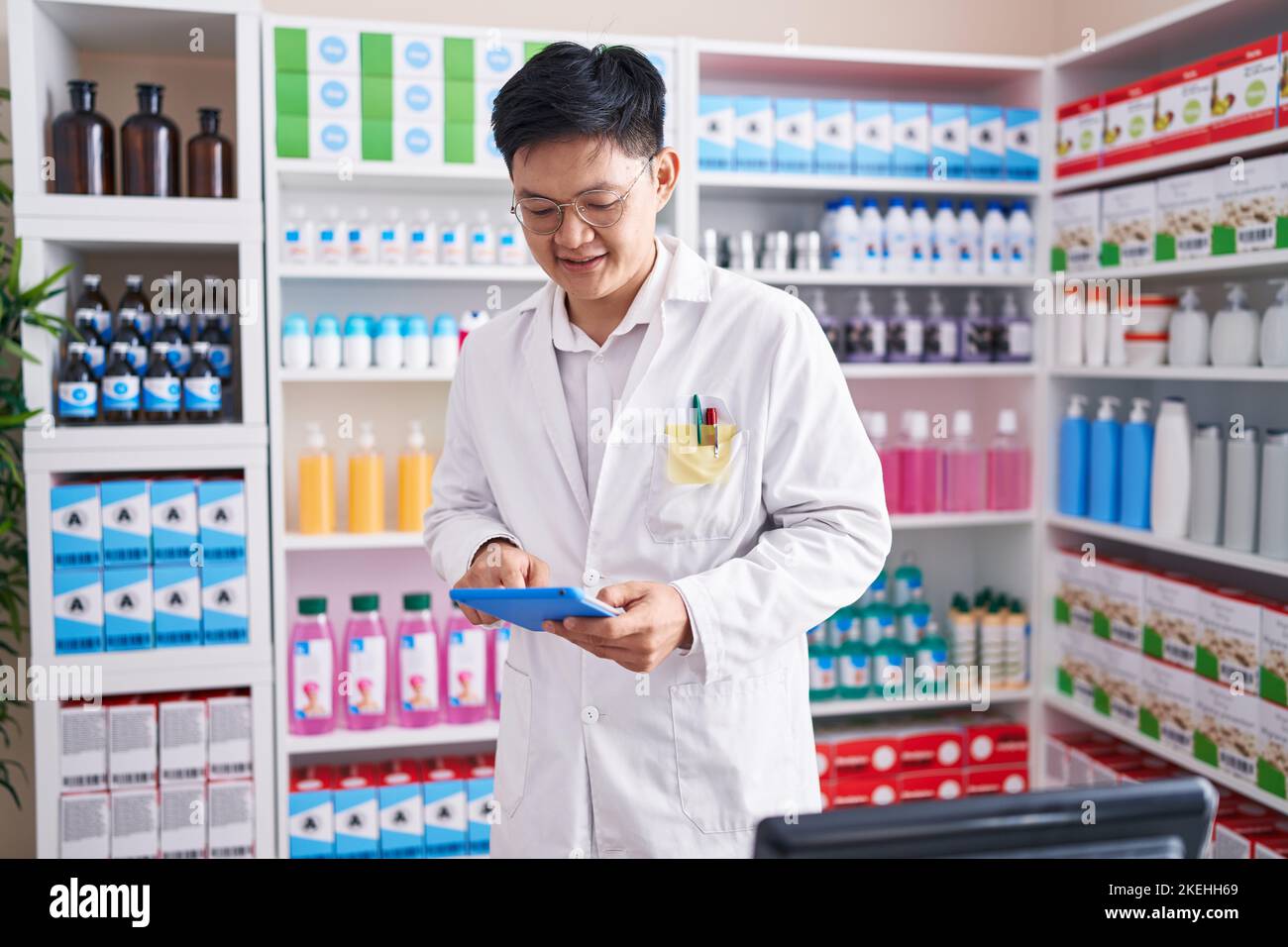 Young chinese man pharmacist using touchpad working at pharmacy Stock ...