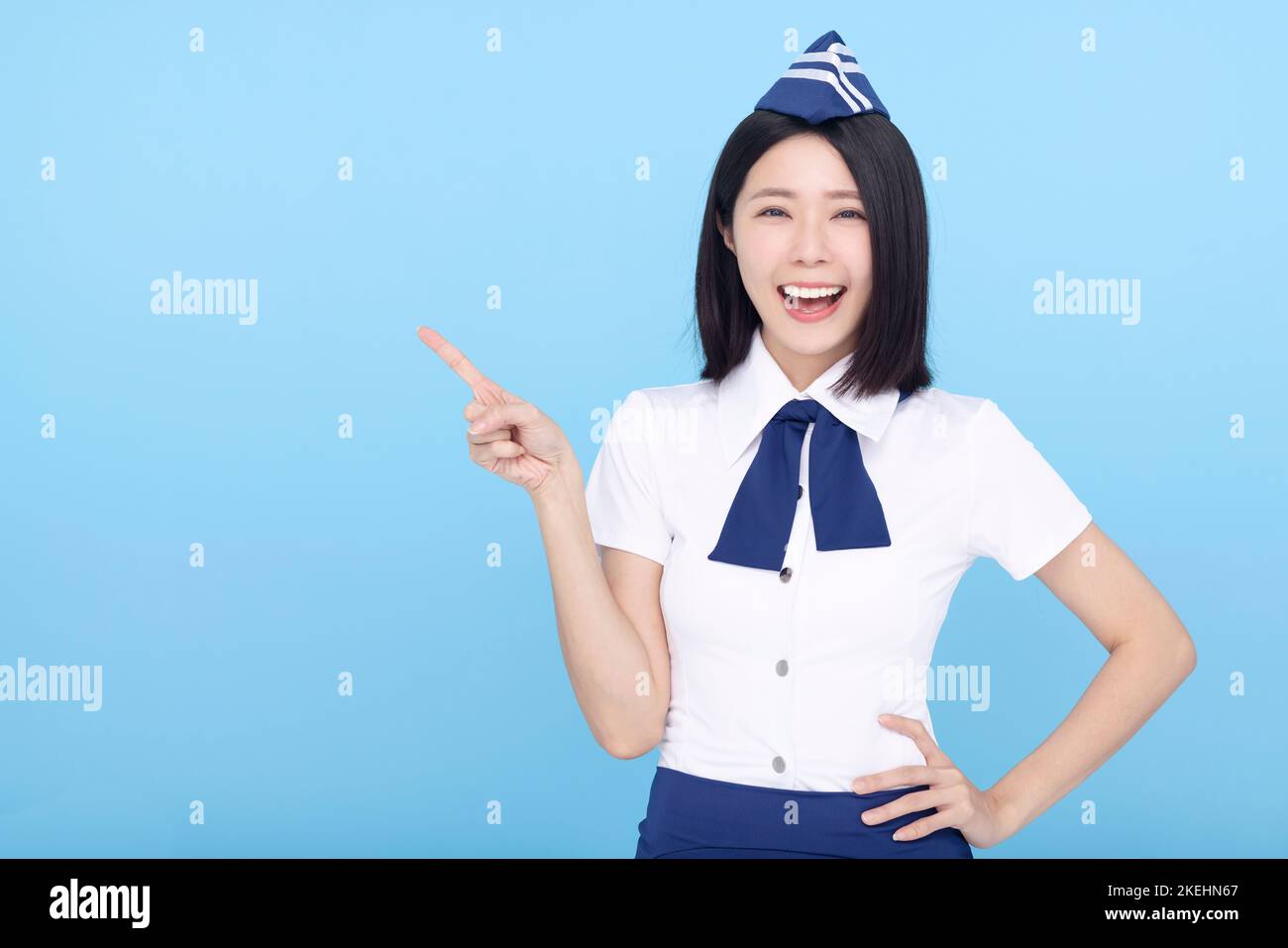 Happy Beautiful Airline stewardess pointing at something on blue background Stock Photo
