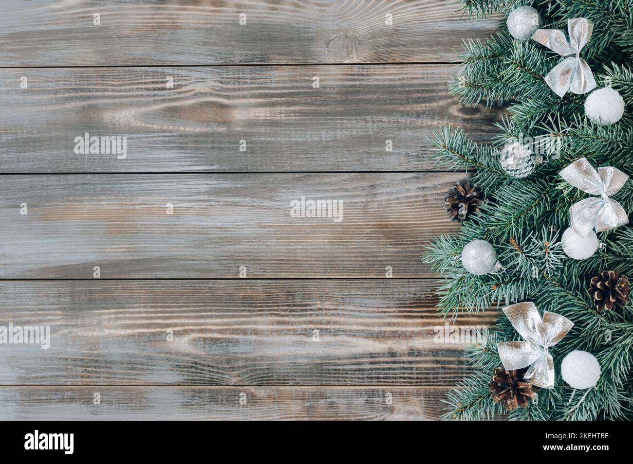 Christmas decorations with silver bows and baubles, cones and fir branches on a wooden background. New Year border. Winter concept. View from above. S Stock Photo