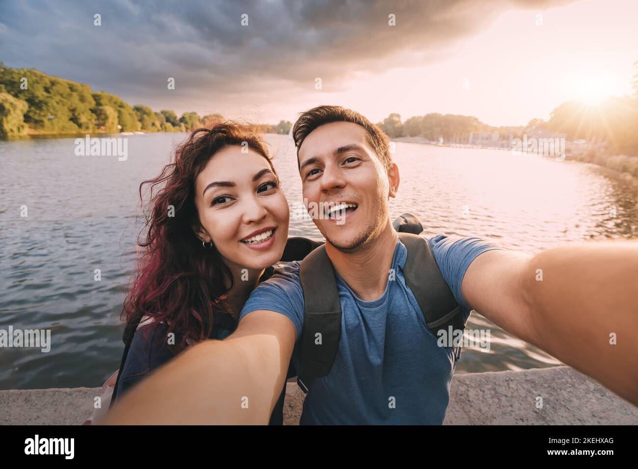 A couple in love or just friends students takes a selfie photo with scenic sunset lake view in city park. Vacation, education and relationship concept Stock Photo