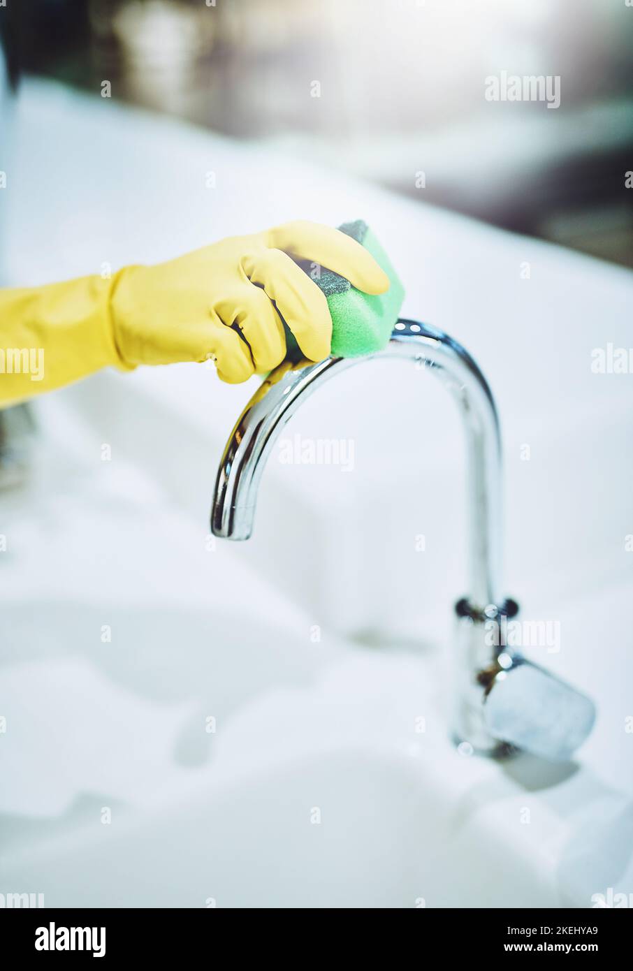 I missed a spot. a unrecognizable person with yellow loves scrubbing a water tap in kitchen. Stock Photo
