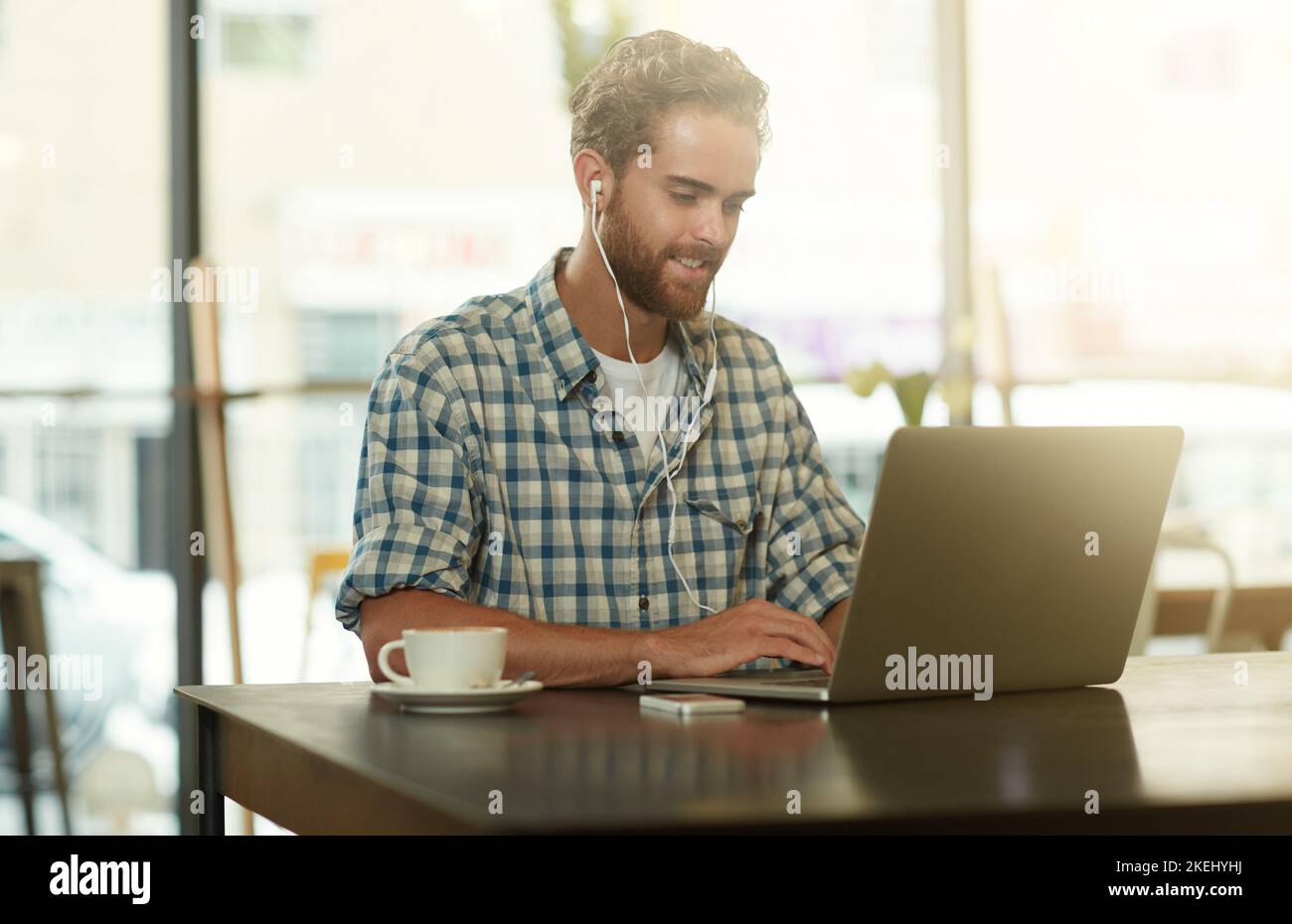Productivity is key. a young man with earphones using a laptop in a cafe. Stock Photo