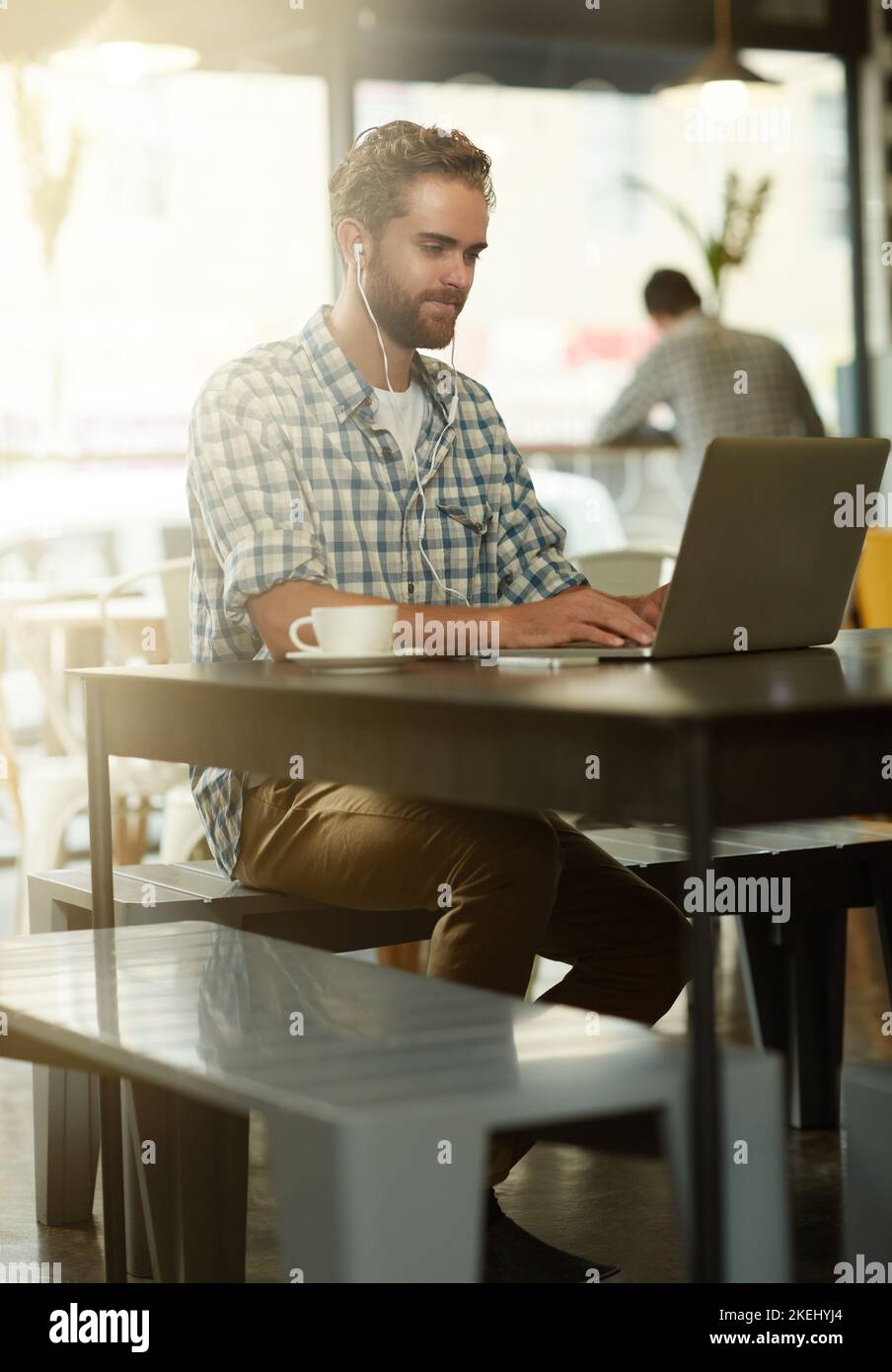 Getting into the flow of things. a young man with earphones using a laptop in a cafe. Stock Photo