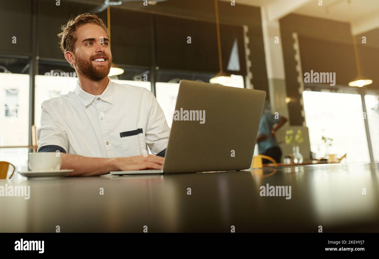 This place has good wifi and great coffee. a young man using a laptop in a cafe. Stock Photo