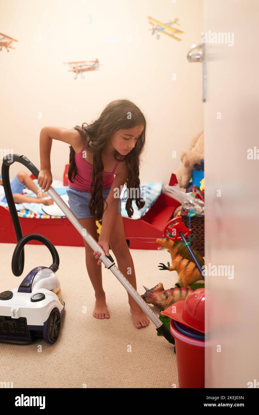 Cleanliness is next to homeliness. a little girl vacuuming her bedroom at home. Stock Photo