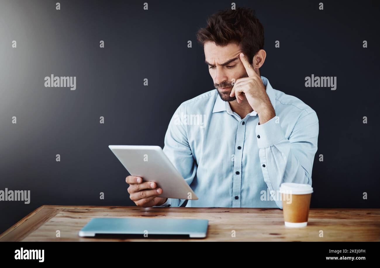 Theres no challenge he cant easily overcome. Studio shot of a handsome young businessman using a digital tablet against a dark background. Stock Photo