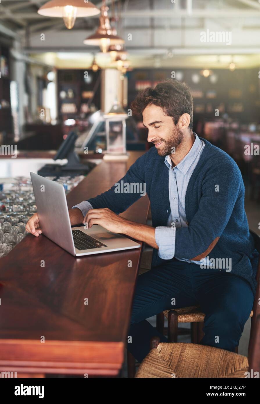 Hes here for the wifi...but the beers not bad either. a handsome young man using his laptop in a bar. Stock Photo