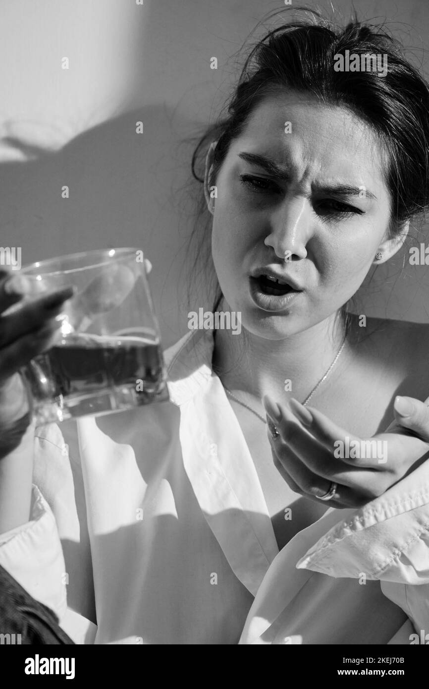 Young woman drinking alcohol from glass against sunny wall background