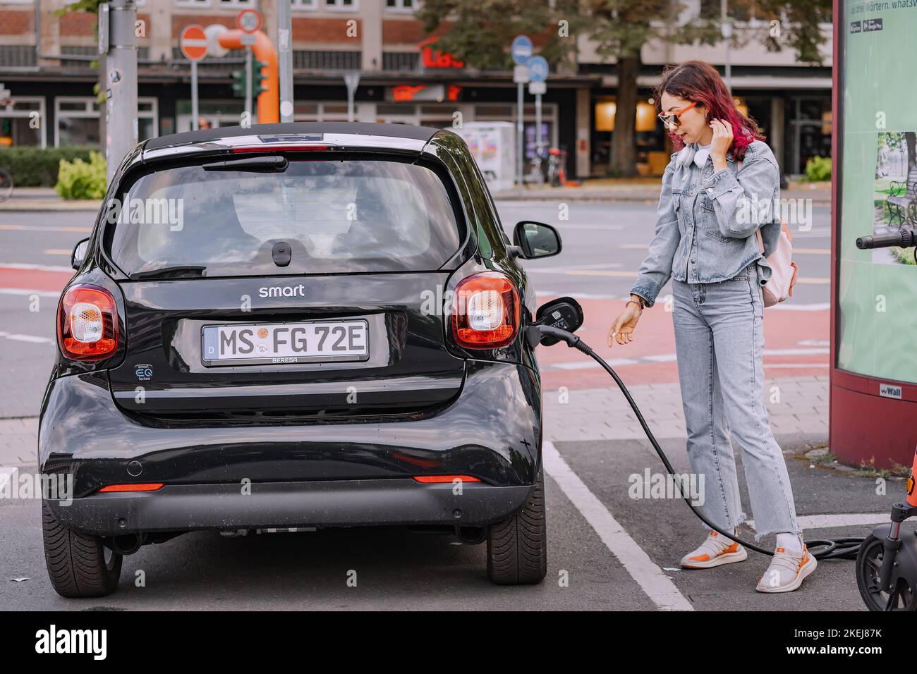 26 July 2022, Munster, Germany: A girl charges her Smart car for two in a free parking lot for eco-electric cars in the city Stock Photo