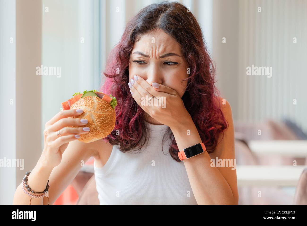 A girl eats a burger in a fast food cafe and feels nausea and heartburn. The concept of