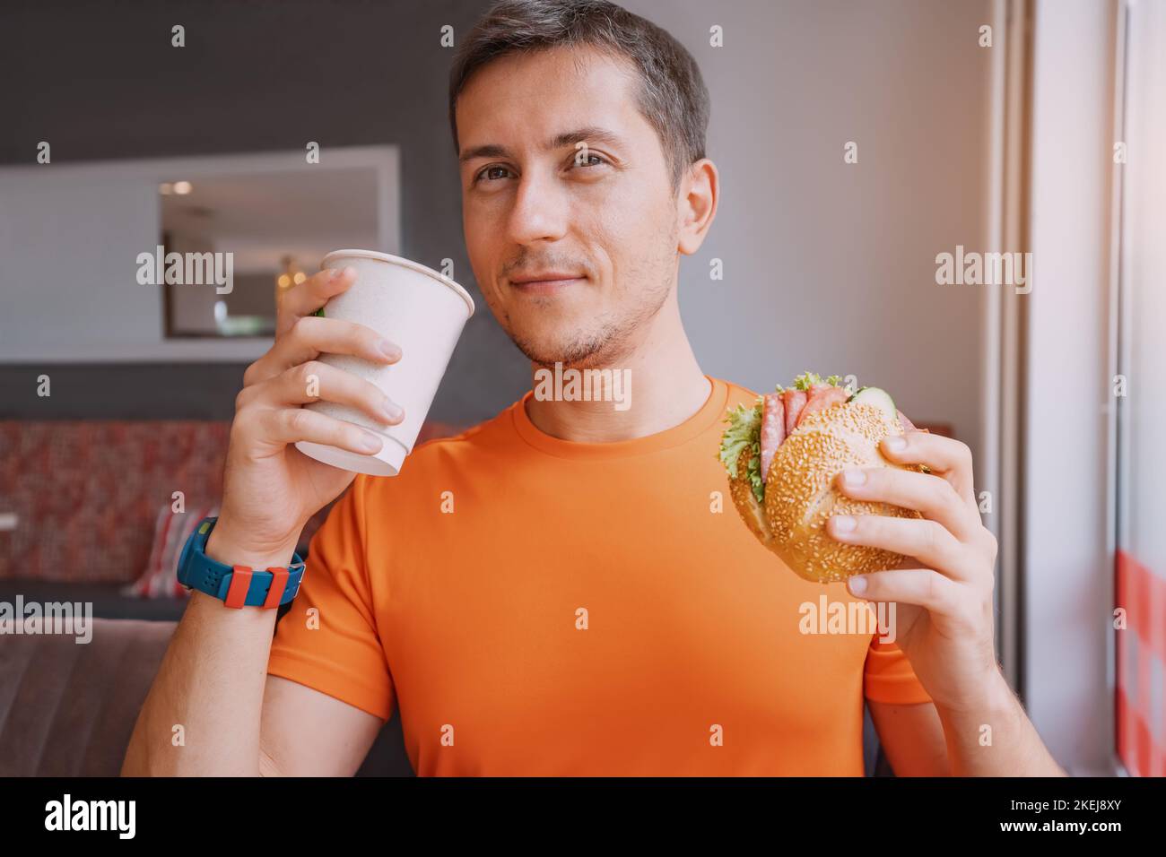 Happy guy drink coffee and eats a hamburger or sandwich with an appetite in a fast food cafe