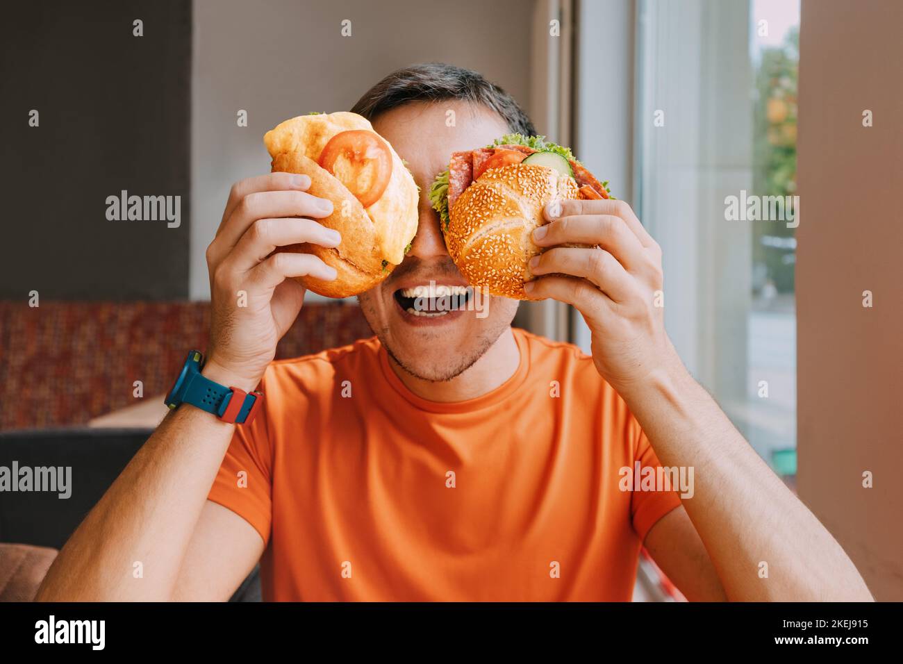 Happy man eating two hamburger or sandwich with an appetite in a fast food cafe. Stock Photo