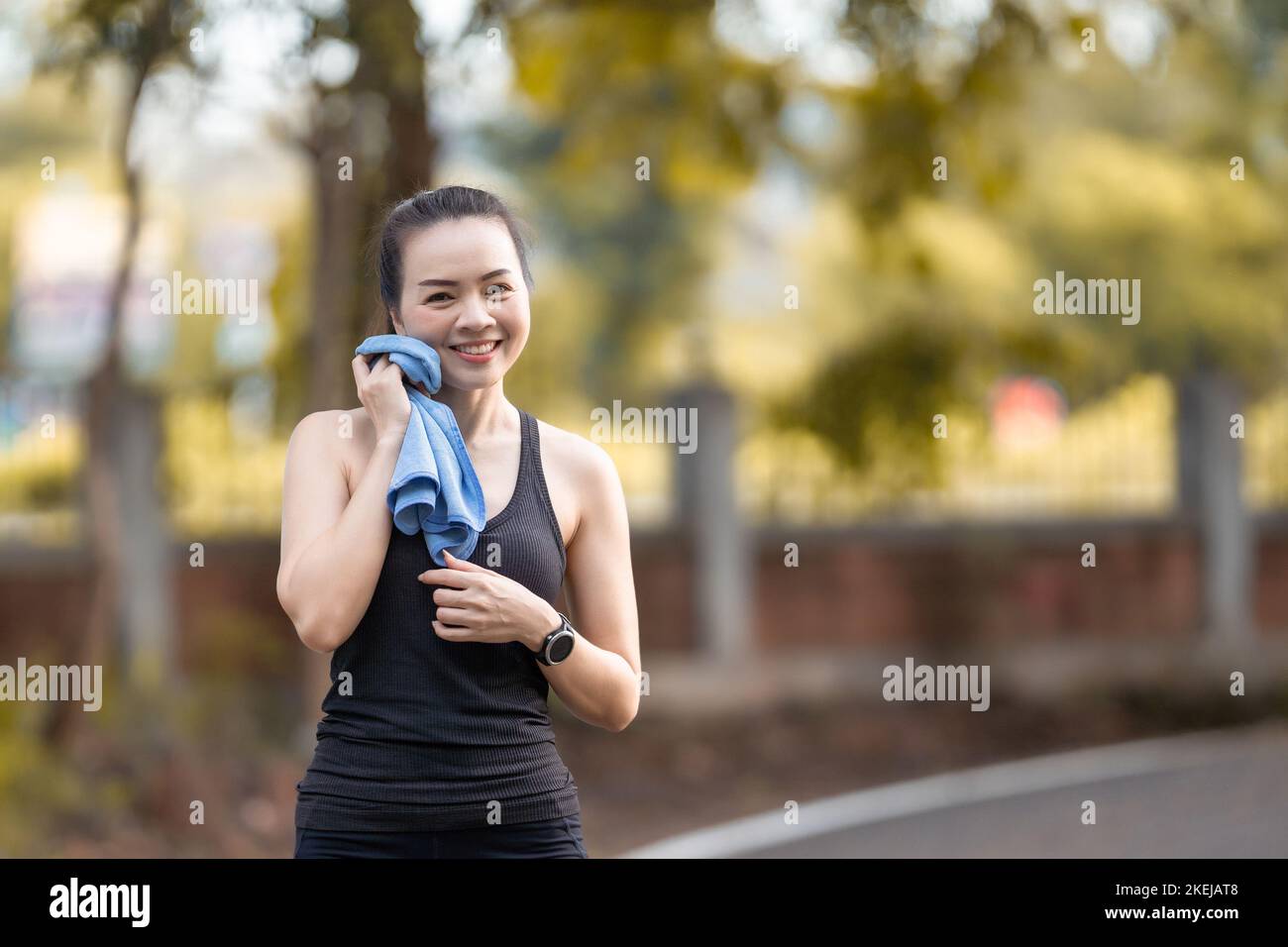 An Asian female in a sports suit on the street, wiping her face with a towel an smiling Stock Photo
