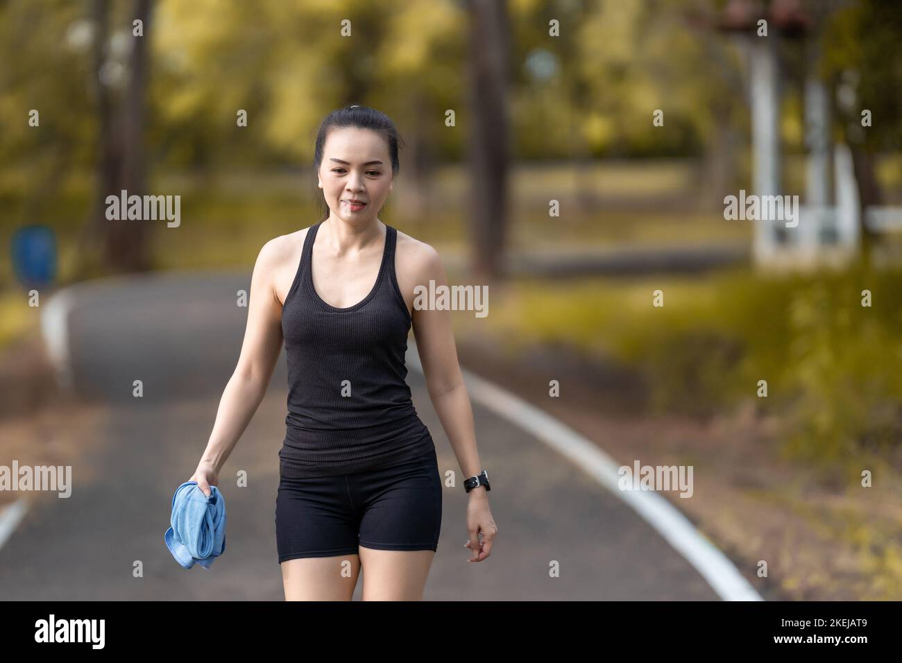 An Asian female in a sports suit jogging on the street, holding a towel in one hand Stock Photo