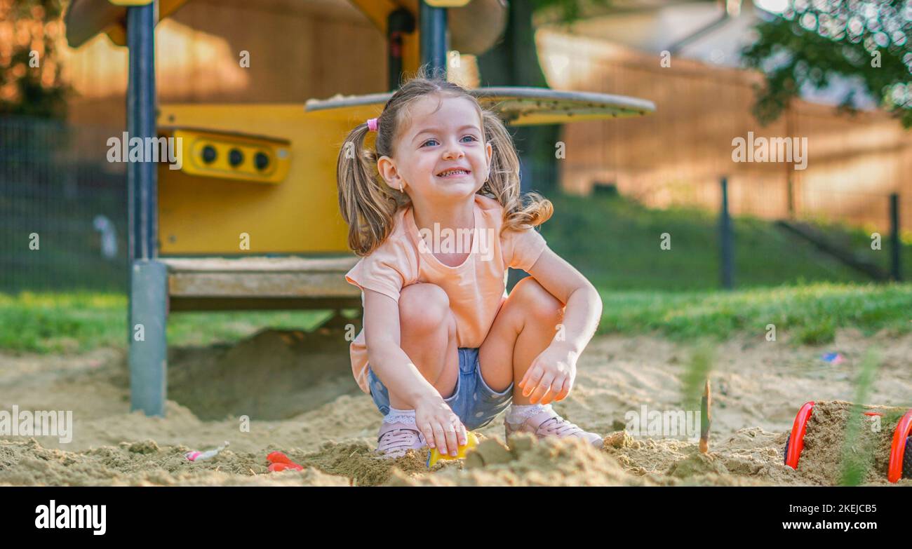 Beautiful baby  having fun on sunny warm summer day - Cute toddler girl playing in sand on outdoor playground Stock Photo