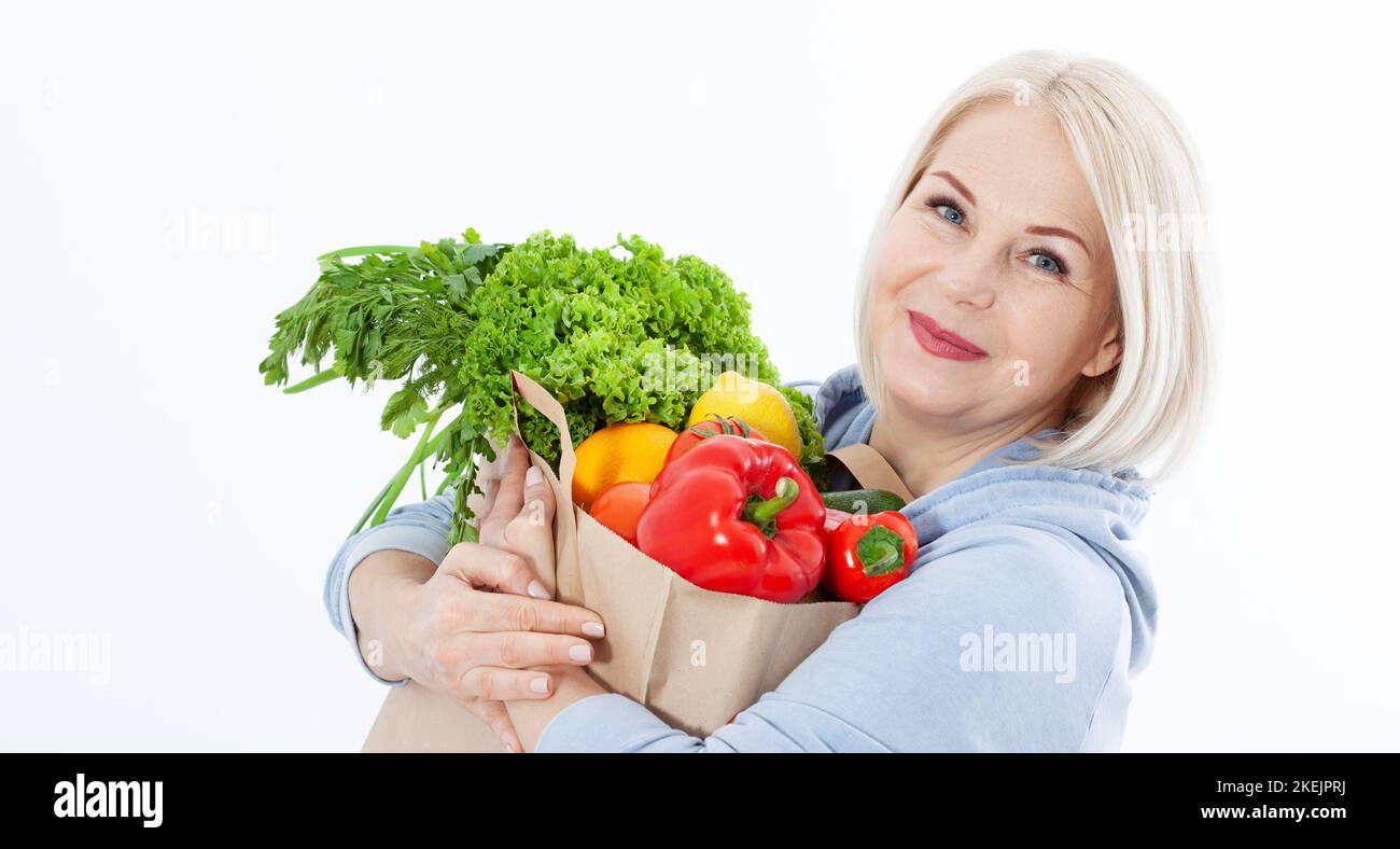 Happy woman with blond hair and beautiful smile holds a bag of vegetables and herbs red pepper and green lettuce in her hands for a healthy diet with Stock Photo