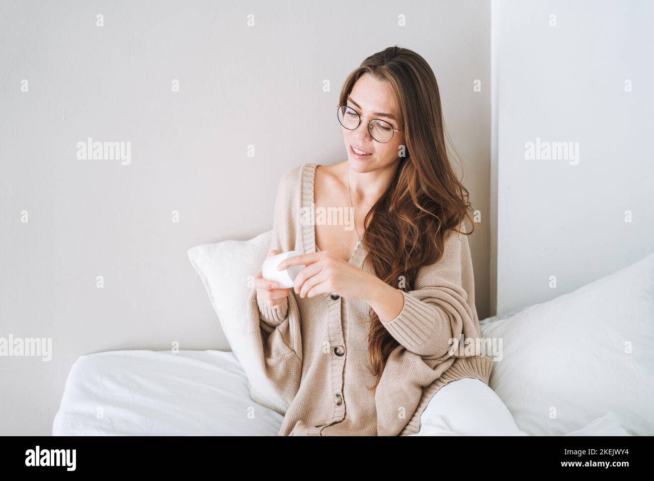 Young woman with long hair in cozy knitted cardigan using cosmetic ...