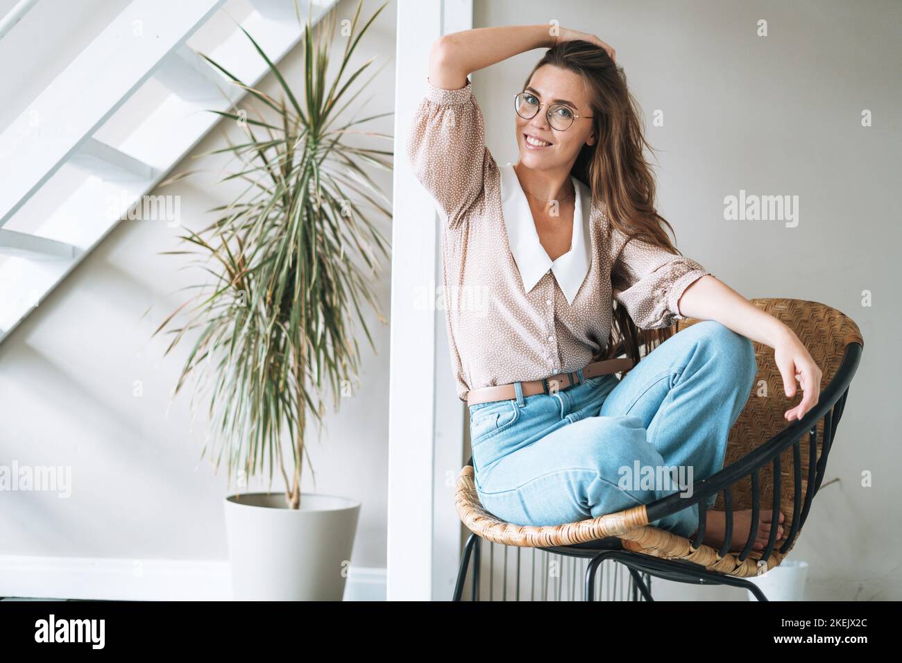 Portrait of young smiling woman with long hair sitting on chair in ...