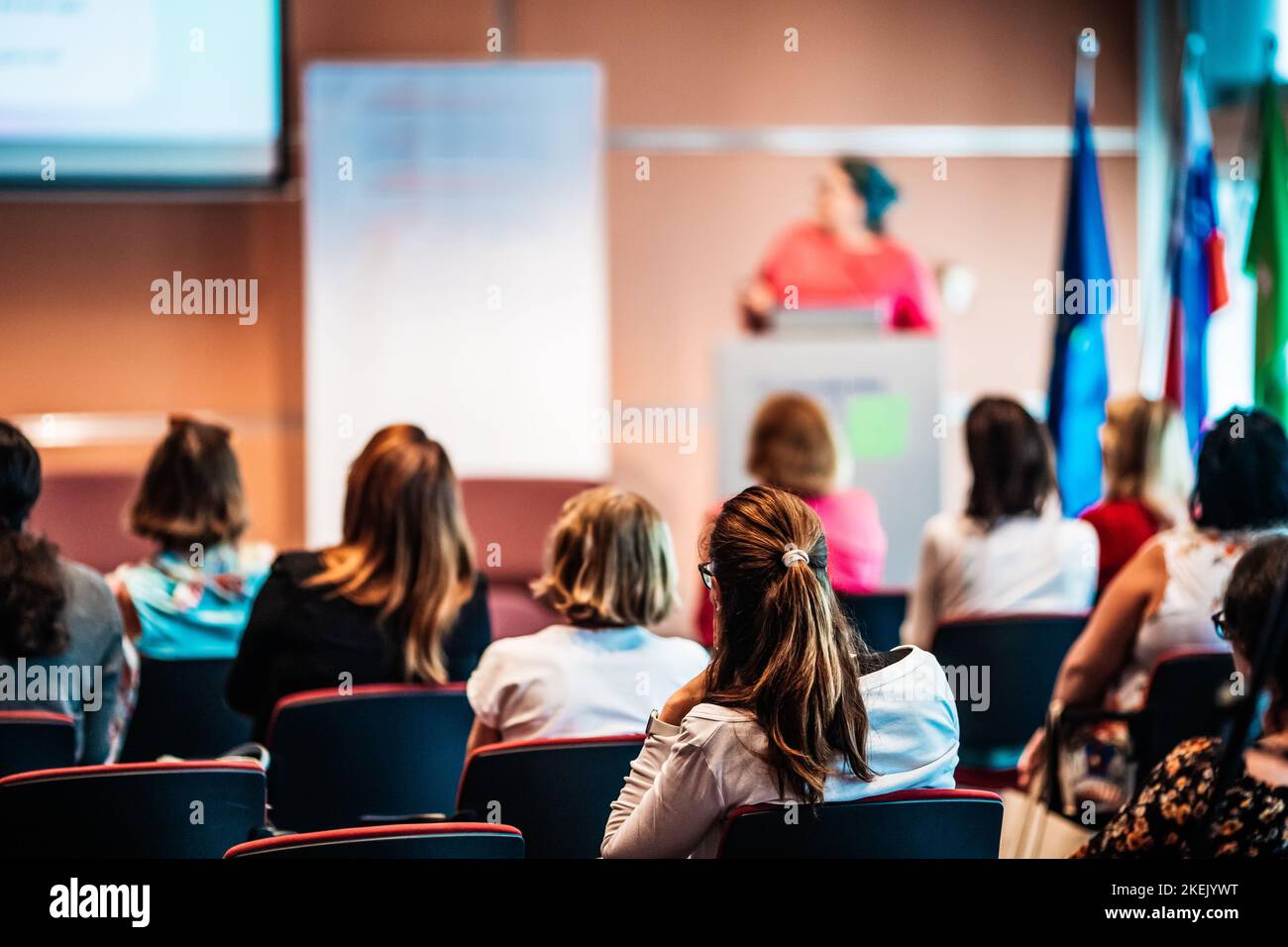Business and entrepreneurship symposium. Female speaker giving a talk at business meeting. Audience in conference hall. Rear view of unrecognized participant in audience. Stock Photo
