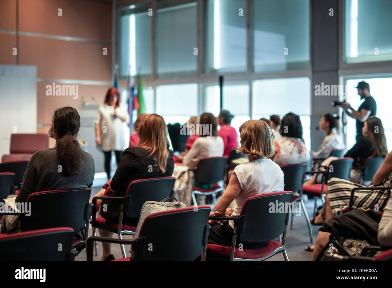 Business and entrepreneurship symposium. Female speaker giving a talk at business meeting. Audience in conference hall. Rear view of unrecognized participant in audience. Stock Photo