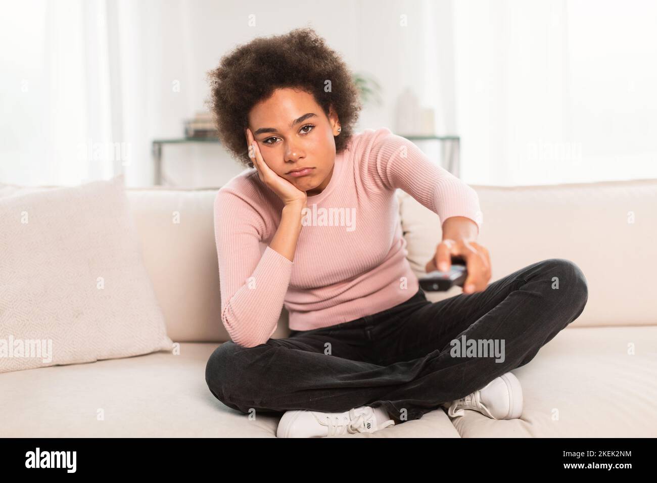Sad bored tired millennial african american woman with remote control watch tv, sit on sofa in living room Stock Photo