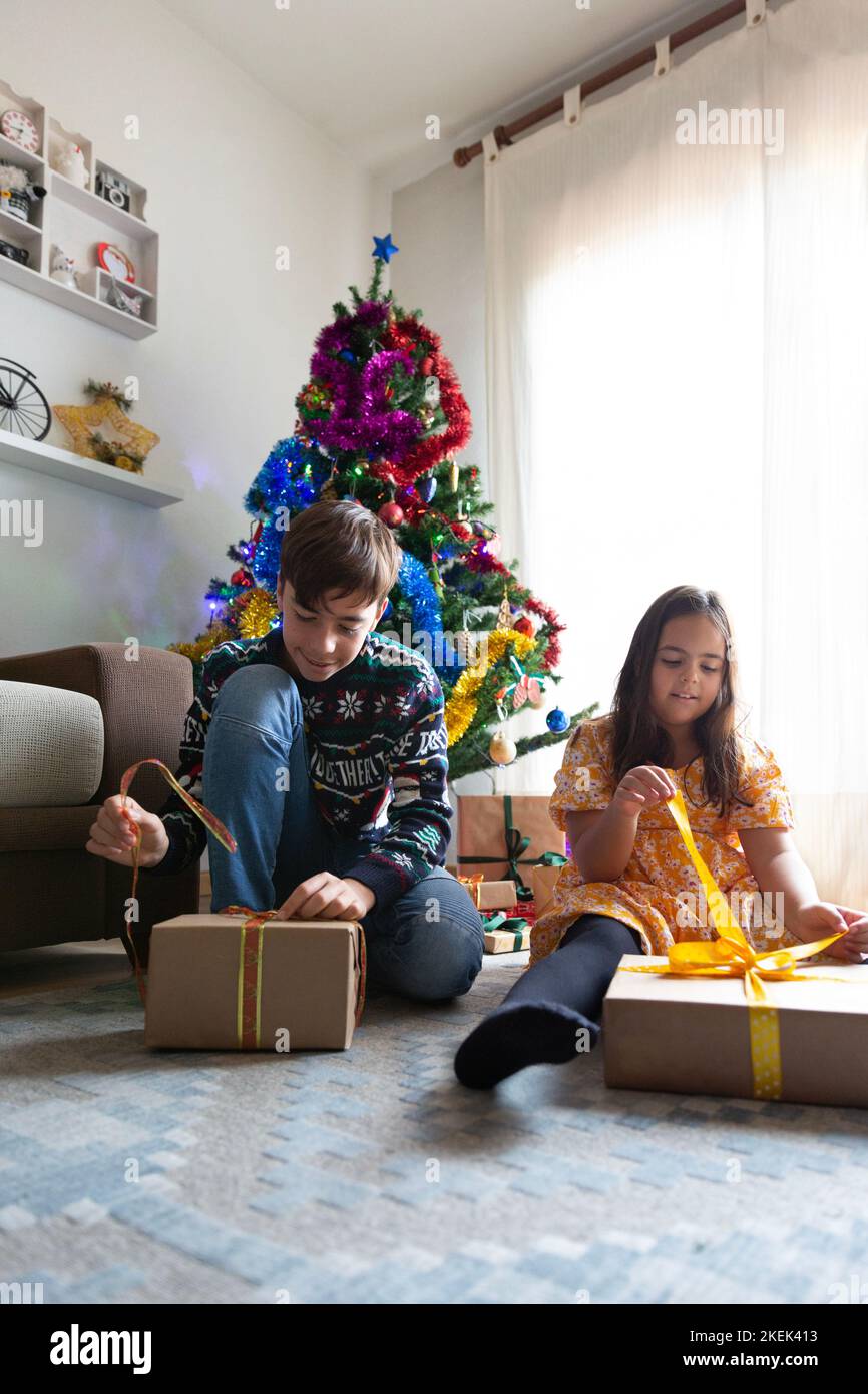 Two Caucasian brothers opening presents at home next to Christmas tree. Space for text. Stock Photo
