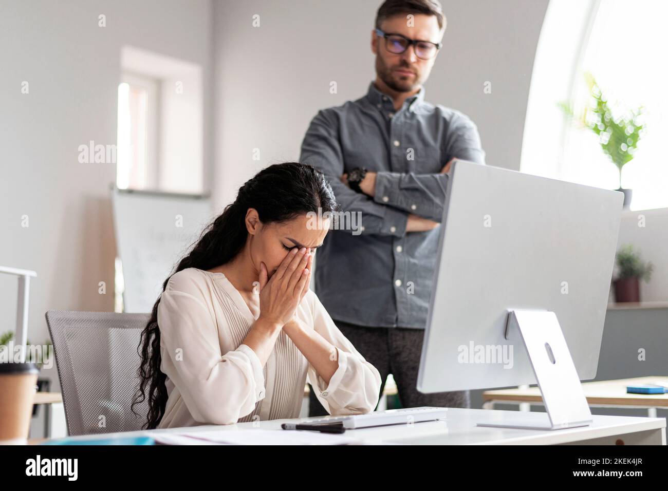 Strict millennial european guy boss look at crying woman manager at workplace with computer, find mistake Stock Photo