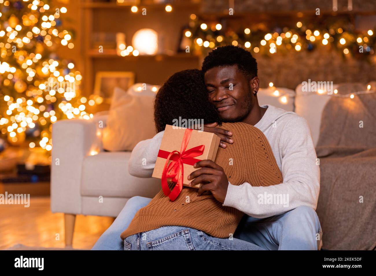 Glad young african american guy hugs wife and hold box with gift near ...