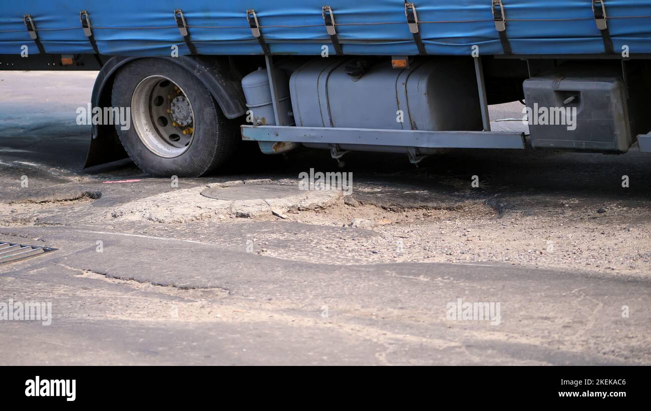 close-up, very poor road coverage, many pits, curved asphalt, a large truck slowly passes a stretch of road in disrepair. the road needs repair. High quality photo Stock Photo