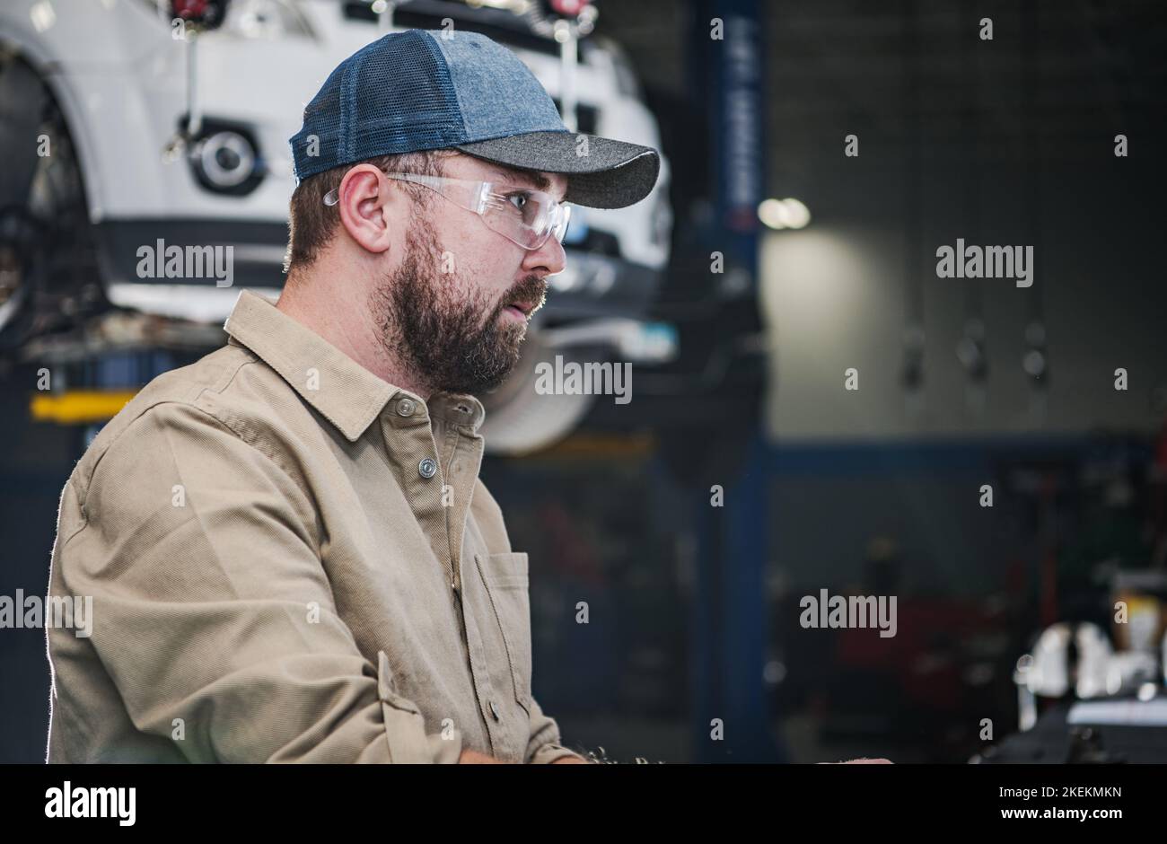 Professional Car Mechanic in His 30s Wearing Eyes Protection Glasses. Automotive Service Center Job. Stock Photo