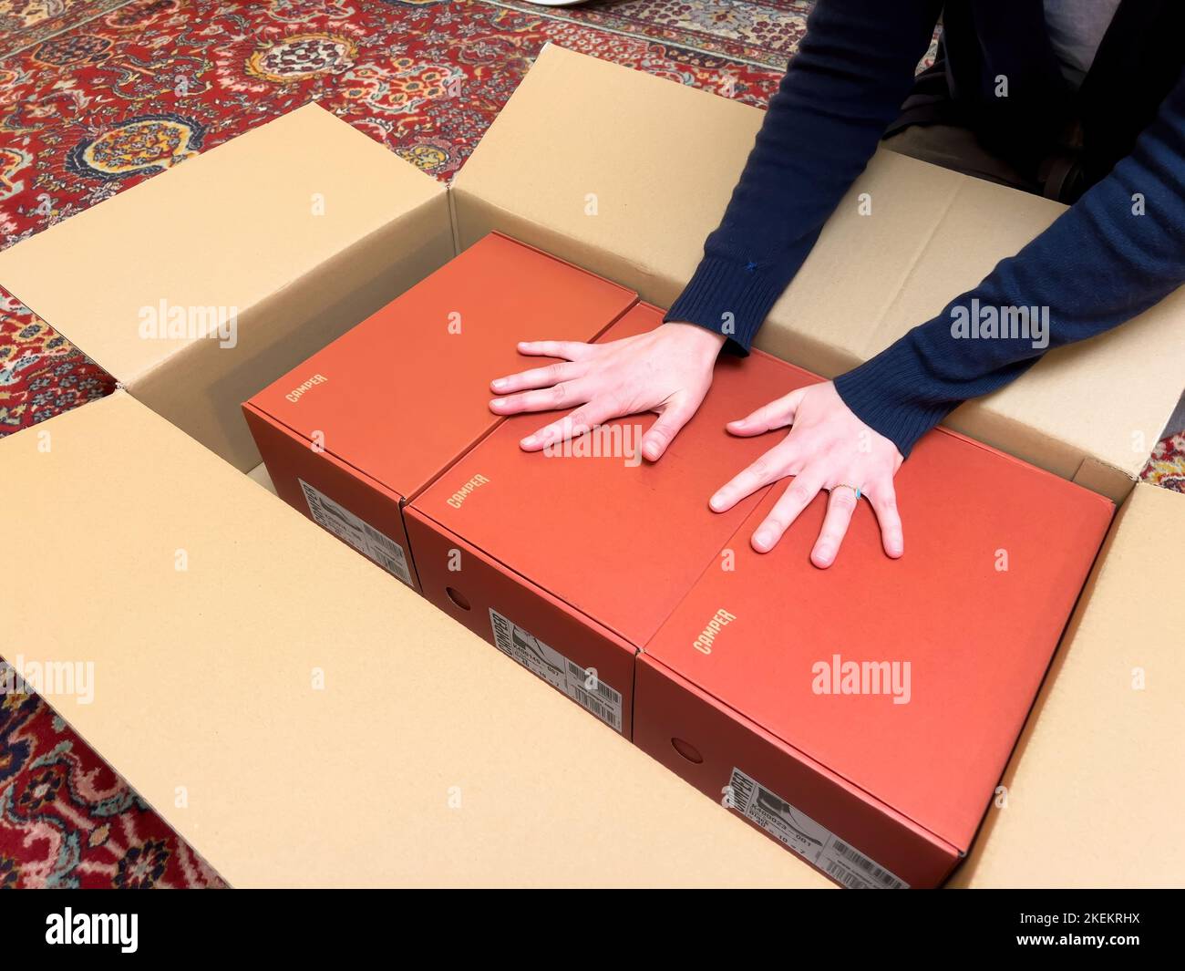 London, United Kingdom - Oct 21, 2022: Woman holding hands Unboxing unpacking cardboard e-commerce internet order with three red Camper shoes Stock Photo