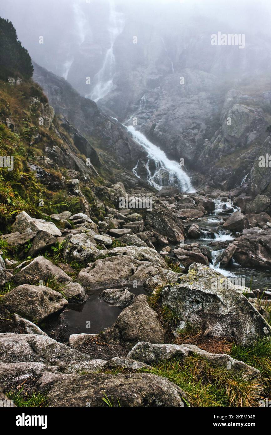 Heavy morning fog covering beautiful mountain waterfall stream going down the creek on a rocky cliff in Tatra national park, Poland Stock Photo