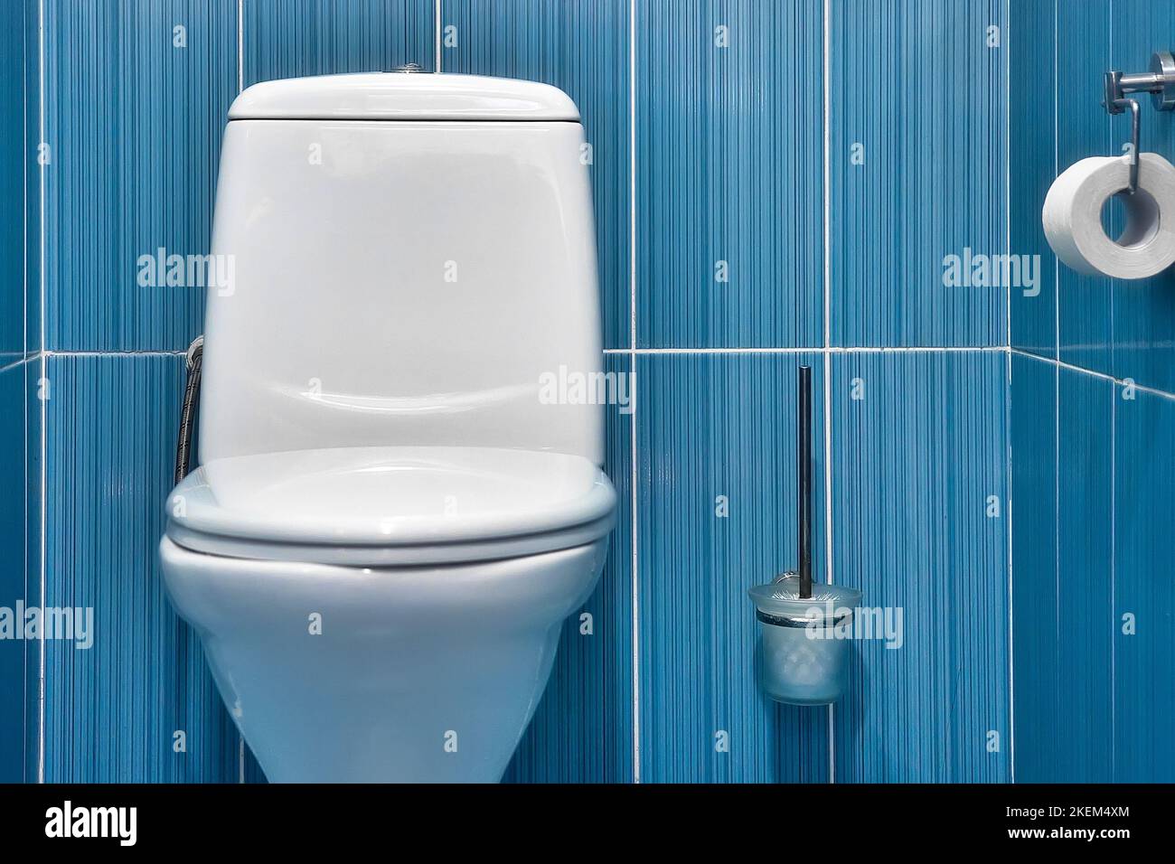View of white toilet with closed lid in toilet with blue tiled wall