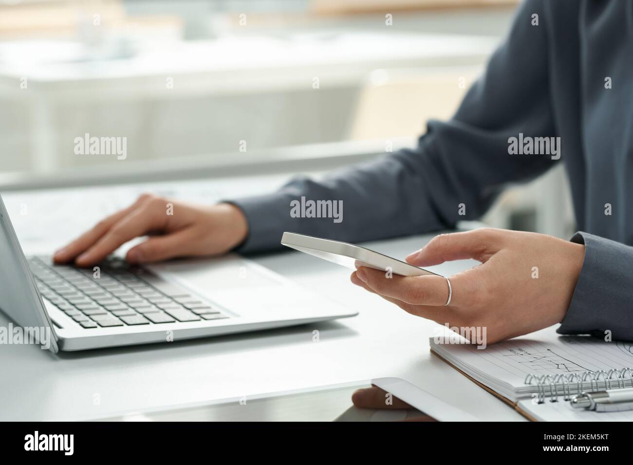 Close-up of young manager using her smartphone while working online on computer at table at office Stock Photo