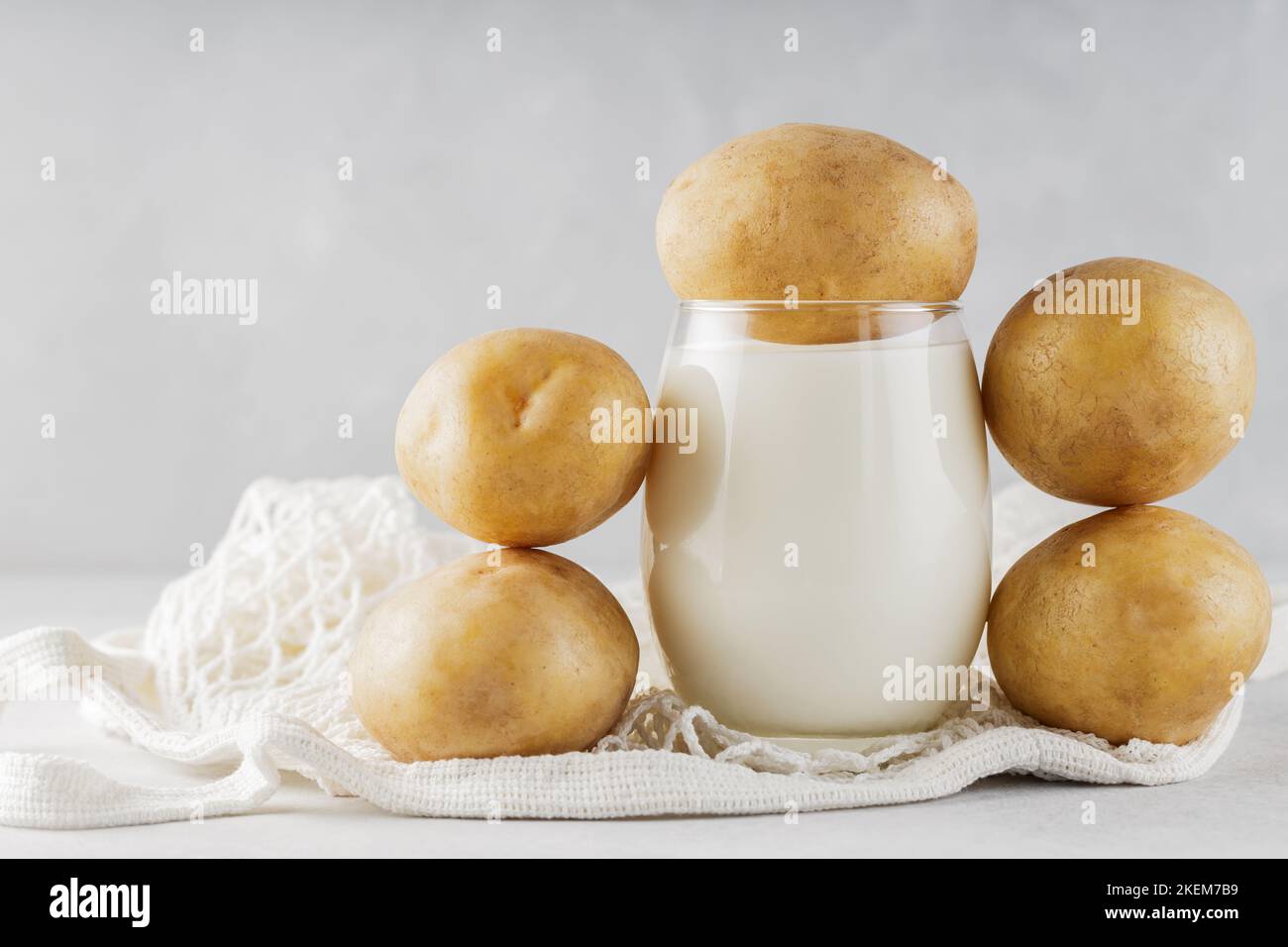 Alternative potato milk in glass and potatoes. Alternative non dairy drink and string bag. Vegan potato milk and sustainable lifestyle concept Stock Photo