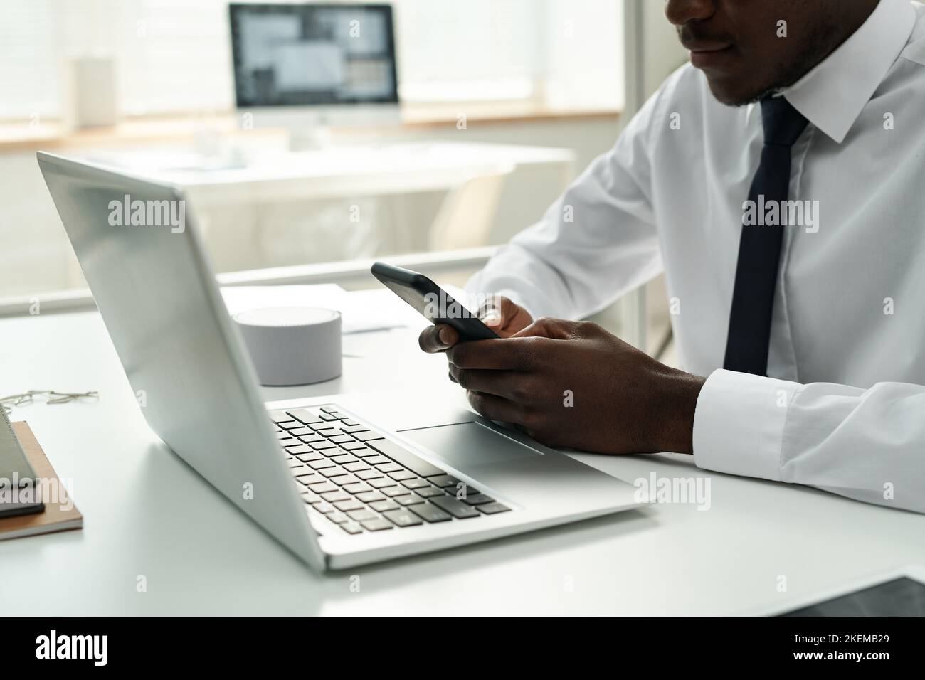 African American businessman typing a message on his smartphone while working on laptop at his workplace at office Stock Photo
