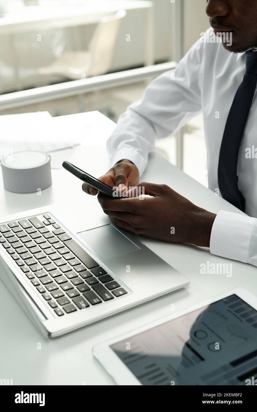 Close-up of African American businessman having online communication on smartphone while working on computer at office Stock Photo