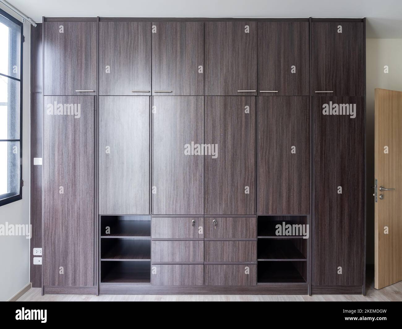 Modern huge brown wooden wardrobe in the white room, closed, front view ...