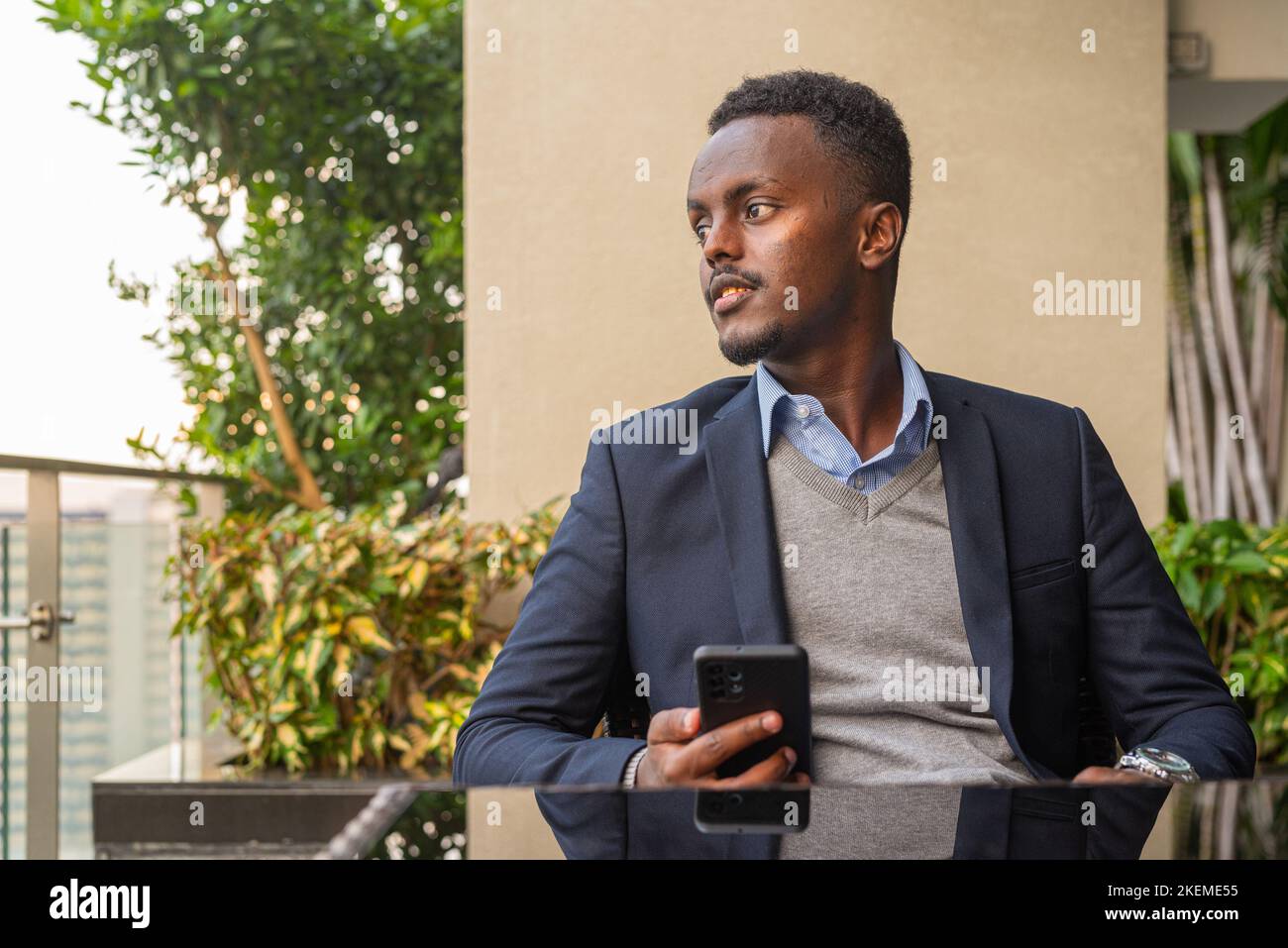 Portrait of handsome black African businessman wearing suit while thinking and using phone Stock Photo